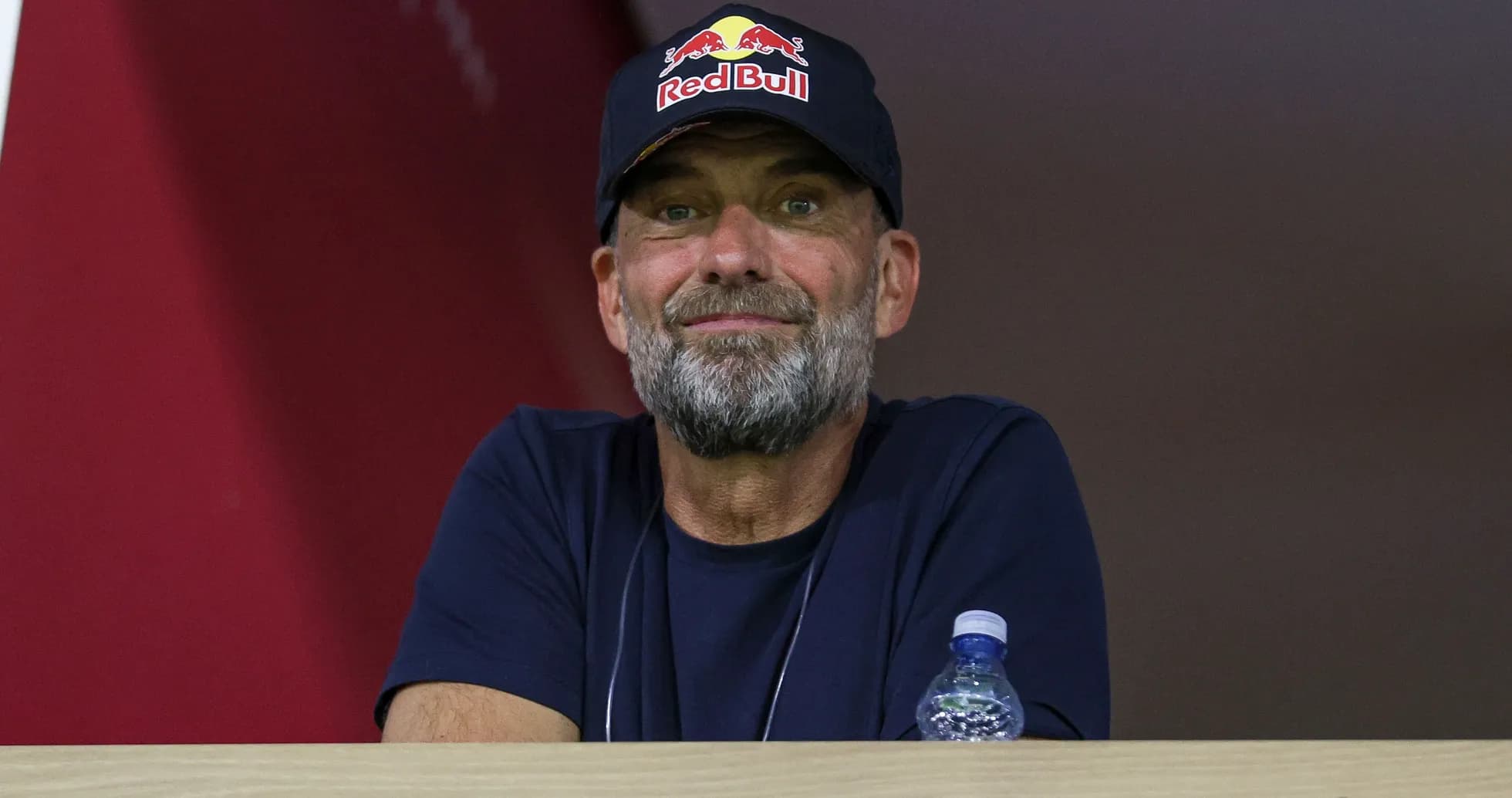 Человек с бородой в кепке Red Bull на трибуне