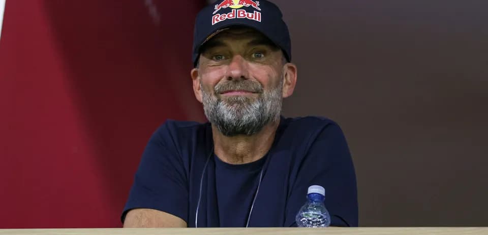 Человек с бородой в кепке Red Bull на трибуне